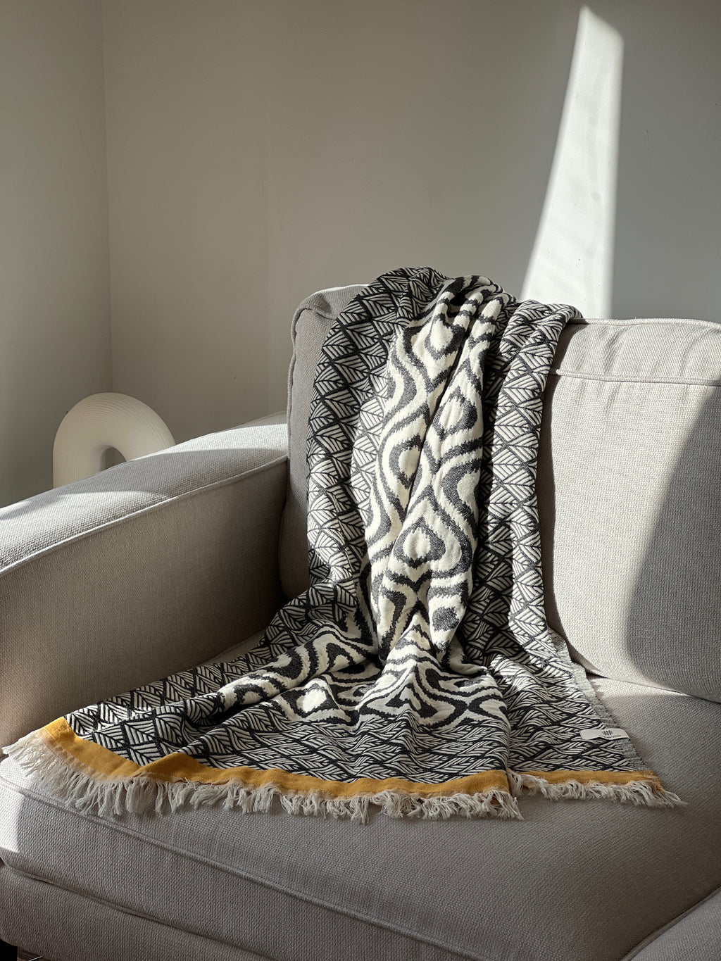 Stylish black and white patterned throw blanket with yellow fringe, perfect for cozy decor.