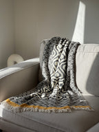Stylish black and white patterned throw blanket with yellow fringe, perfect for cozy decor.
