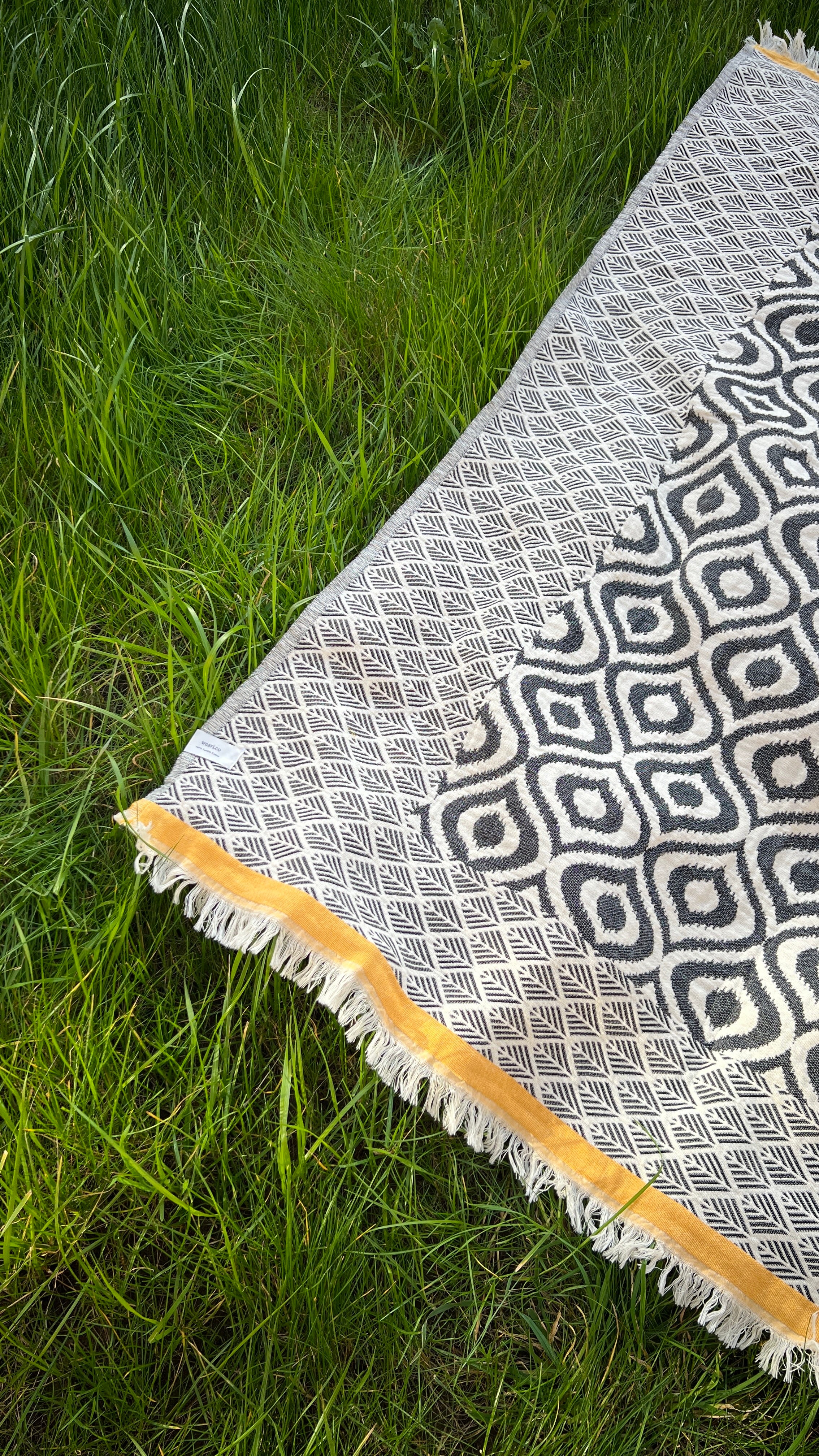 Bohemian-style area rug, black and white geometric patterns, fringed edges with mustard yellow trim.