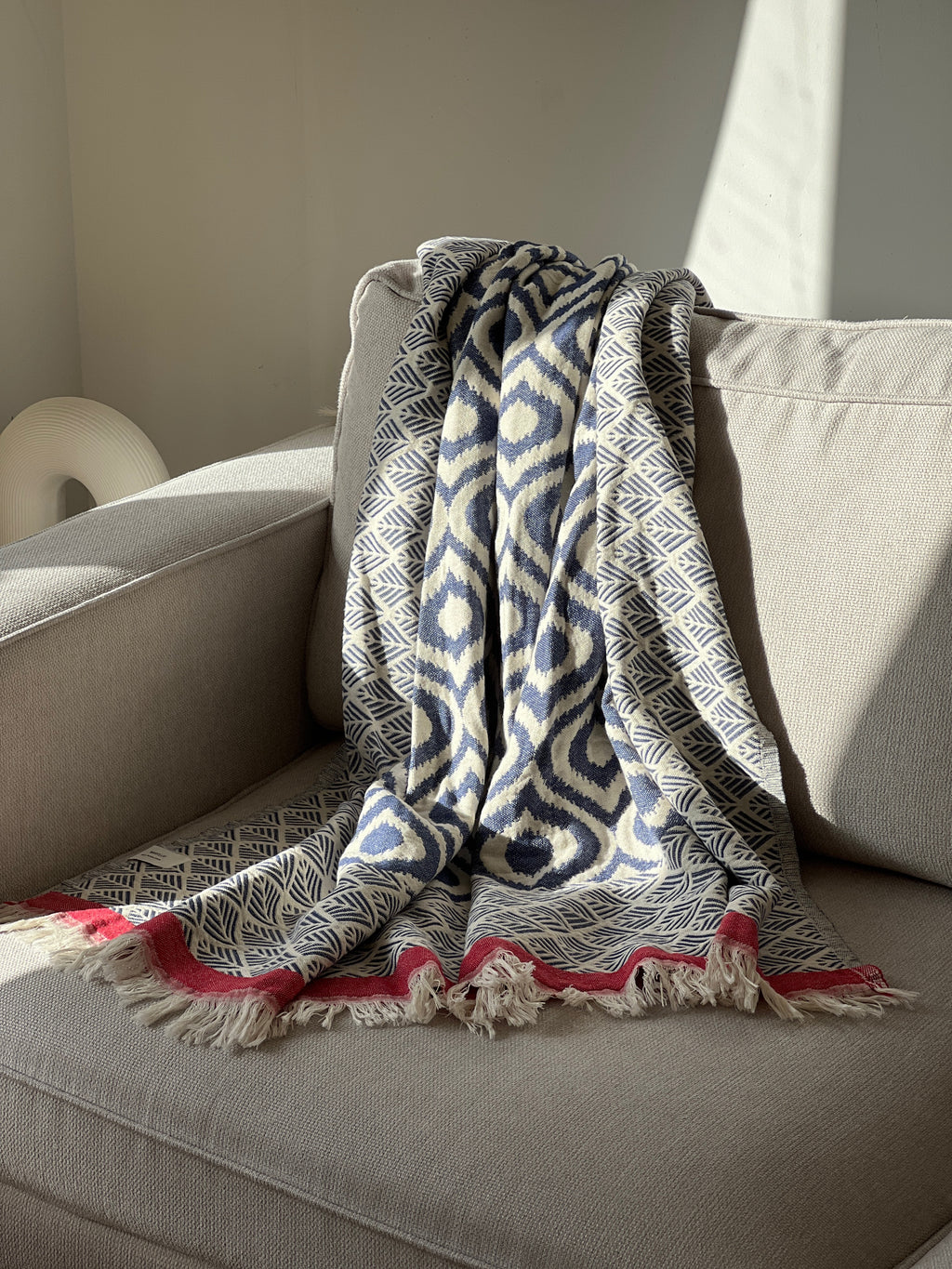 Navy and white patterned cotton throw blanket with red fringe, perfect for cozying up on a sofa.