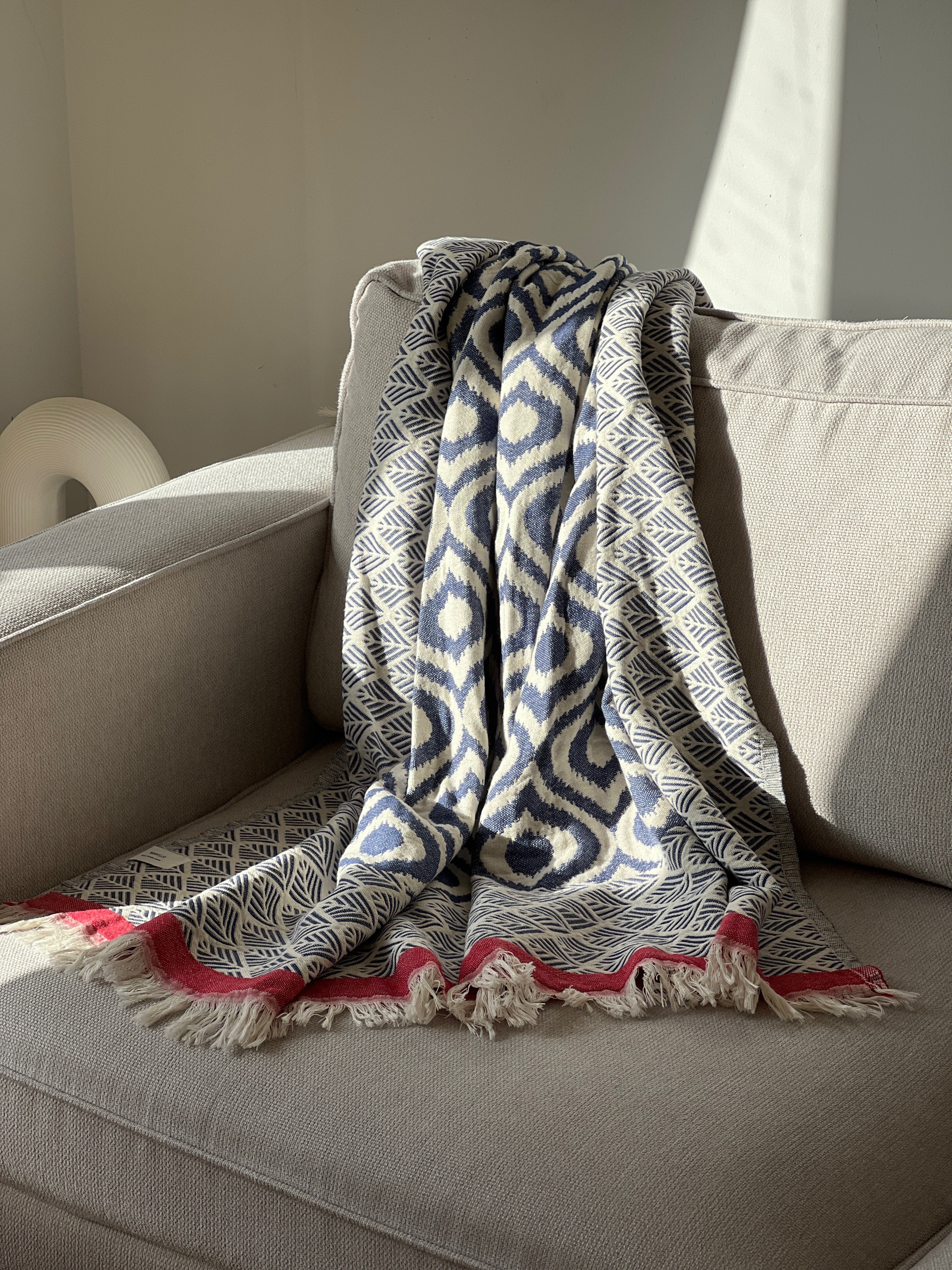 Navy and white patterned cotton throw blanket with red fringe, perfect for cozying up on a sofa.