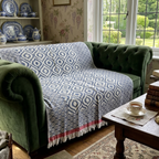 Navy and white patterned throw blanket on green chesterfield sofa, featuring fringe detail and cozy design.